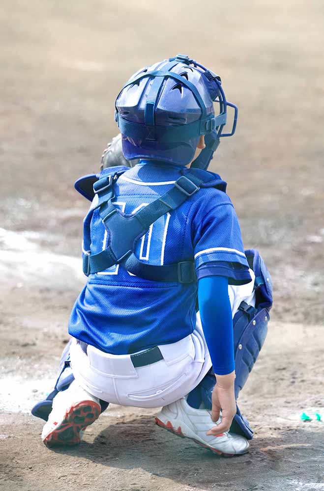 A boy baseball catcher waits in position for the next pitch.