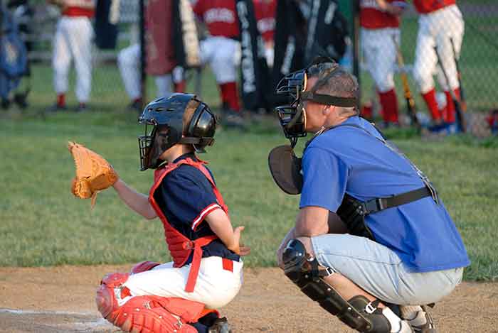 Youth catcher in position behind home plate, glove out, ready for the pitch. Adult umpire crouches behind him.